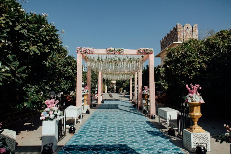 Beautifully decorated outdoor wedding aisle with floral arrangements and draped canopy on a sunny day.